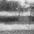 raindrops on a window pane and screen obscuring a view of high banks of dirty snow, a street lamp, a tree, and a house across the street hung with dangerously long icicles
